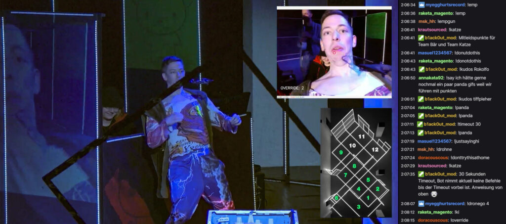Screenshot des Twitch-Streams einer Show von 2022. Rechts der Chat, links HJotti im Bühnenbild, wie er sich vor einer heranfliegenden Drohne zurückbiegt. Bild im Bild der Kamerafeed der Drohne.